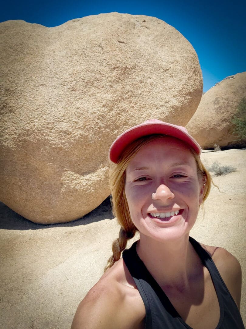 A woman with red hat and braid standing in front of large rocks.